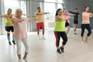 Grupo de personas de diferentes edades disfrutando de una clase de aeróbicos para Adelgazar en un gimnasio, realizando movimientos coordinados con sonrisas y energía.