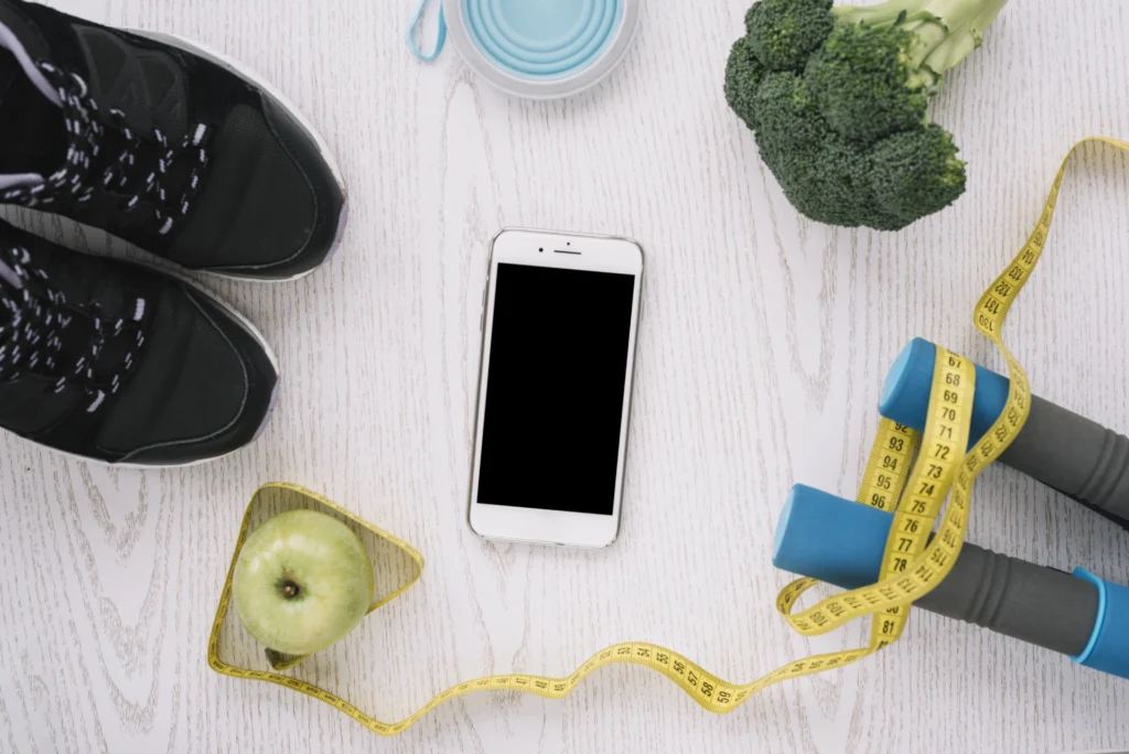 Elementos para un estilo de vida saludable, incluyendo tenis, pesas, frutas y una cinta métrica, representando los beneficios del Balón Gástrico Ingerible en Duitama.