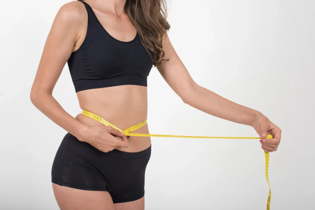 Mujer en ropa deportiva midiendo su cintura con una cinta métrica, representando pérdida de peso y bienestar que logro con la Manga Gástrica en Valledupar.