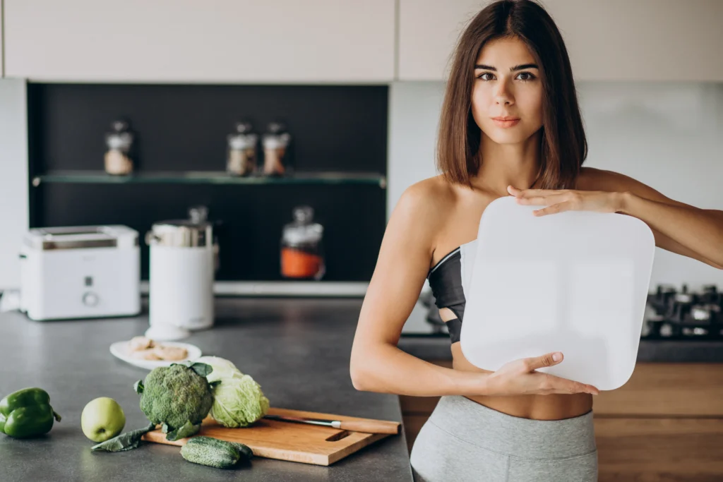 Mujer en cocina saludable sosteniendo una báscula, representando el éxito en la pérdida de peso tras la Manga Gástrica en Floridablanca.