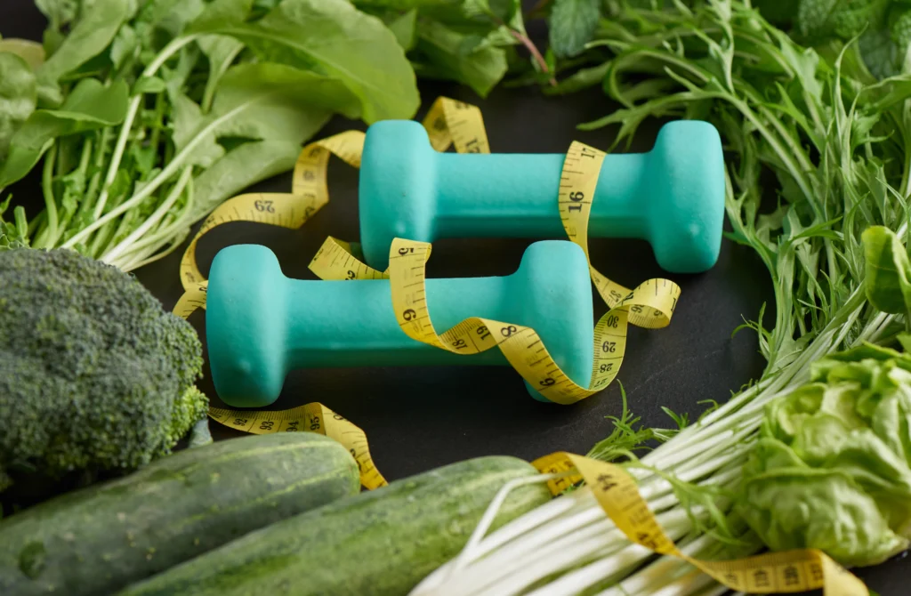 Pesas, cinta métrica y vegetales verdes, simbolizando la combinación de ejercicio y alimentación saludable tras la Manga gástrica en Sogamoso.