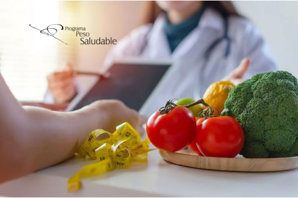 Consulta médica del Programa Peso Saludable con frutas y verduras frescas sobre la mesa, simbolizando una alimentación balanceada y el acompañamiento clínico personalizado para el control de peso.