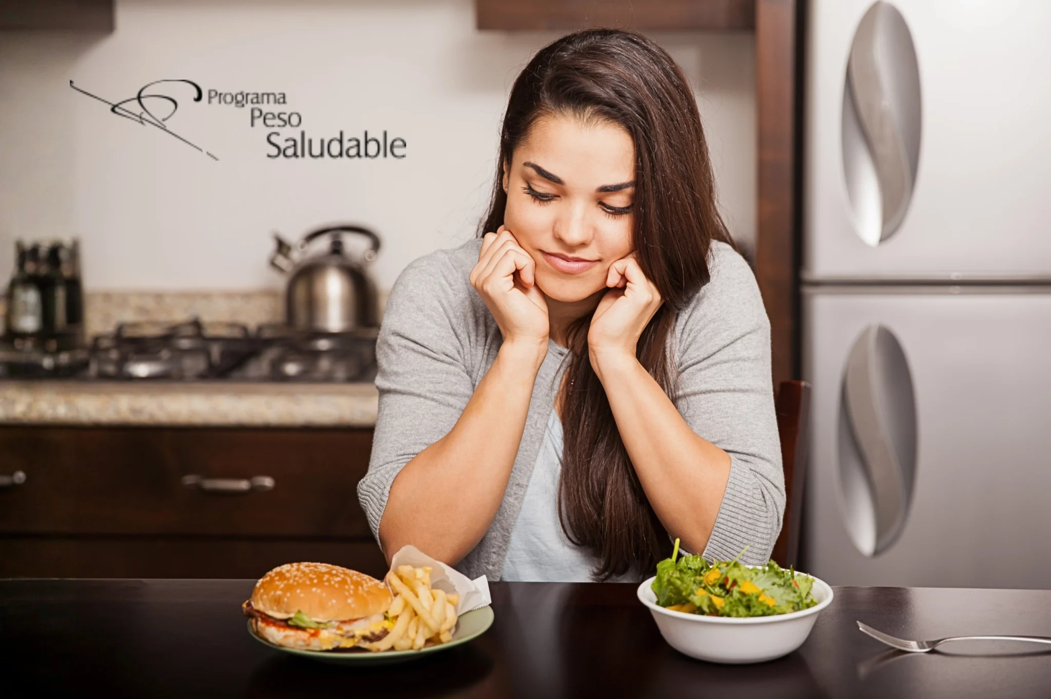 Mujer sentada frente a una mesa en la cocina, observando con duda dos opciones de comida: una hamburguesa con papas fritas y una ensalada fresca. En el fondo se ve una estufa, una tetera y el logotipo de “Programa Peso Saludable” en la pared.